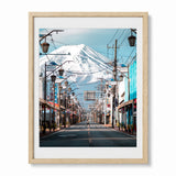 A framed photographic art print of a Japanese street scene with mount Fuji in the background, shown in a light wood frame against a plain white wall.