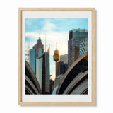 Framed art print of a Sydney skyline photograph, featuring the Sydney Tower and modern skyscrapers, in a light natural wood frame with a white mat.