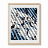 A framed art print featuring an aerial photograph of people crossing Shibuya Crossing in Japan, presented in a light natural wood frame with a white mat against a white background.