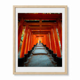 Framed wall art featuring a photograph of a pathway lined with bright orange torii gates, shown in a light wood frame with a white mat against a white background.