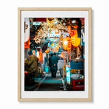 A framed photographic art print of a Japanese street scene at night, featuring warm orange lanterns, a person walking away in Tokyo's memory lane, set in a light wood frame with a white mat.