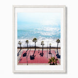 Framed wall art featuring an aerial photograph of a red basketball court at capistrano beach, with palm trees casting long shadows. Set in a white frame with a white mat.