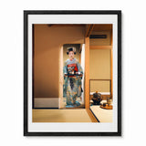 A framed art print featuring a traditional Japanese woman in a blue and red kimono standing in a tatami room, presented in a black frame with a white mat.