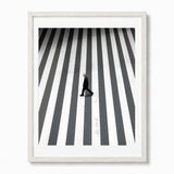 Framed wall art featuring a high-angle black and white photograph of a man walking across a zebra crossing, set in a white wood frame against a white background.
