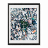 A framed aerial photograph of a Hong Kong urban cityscape with a central green park and an airplane, presented in a black frame with a white mat against a light gray background.
