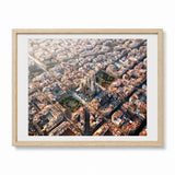 A framed aerial photograph of a dense Barcelona cityscape with a prominent cathedral at the center, shown in a light natural wood frame with a white mat against a clean white background.