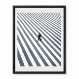 Framed wall art featuring a high-angle black and white photograph of a man walking across a striped crosswalk, presented in a black frame with a white mat against a light gray background.
