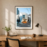 A wall art print of a small house in Tokyo Japan with an orange car parked in front, presented in a black frame and hanging on a wall in an office space