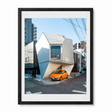 A photograph of a small house in Tokyo Japan with an orange car parked in front, presented in a black frame with a white mat against a light gray background.