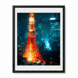 Framed wall art featuring a nighttime cityscape with the Tokyo Tower illuminated in orange-red tones against a dark blue and teal skyline, shown in a black frame with white mat on a light gray background.