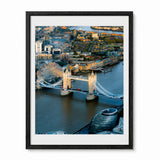 A framed photographic art print of London, featuring a high-angle view of Tower Bridge over the Thames with the City of London skyline, including the London Eye, set in a black frame with a white mat.