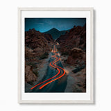 A framed vertical art print depicting a winding road through the Valley of Fire State Park in Nevada. The print is enclosed in a white frame.