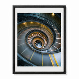 A framed art print featuring a high-angle photograph of the famous bramante staircase in Vatican City, enclosed in a black frame.