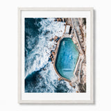A framed aerial photograph of a bronte baths at an Australian coastal beach, presented in a white wood frame with a white mat against a light gray background.