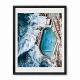 A framed aerial photograph of a bronte baths at an Australian coastal beach, presented in a black frame with a white mat against a light gray background.