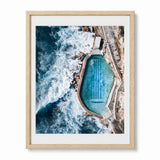 A framed aerial photograph of a bronte baths at an Australian coastal beach, presented in a light wood frame with a white mat against a light gray background.