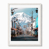A framed photographic art print of a Japanese street scene with mount Fuji in the background, in a white woo frame shown against a plain white wall.