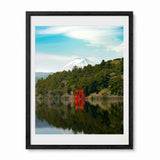 A framed art print featuring a scenic landscape of Mount Fuji reflected in a calm lake, with a bright red torii gate in the foreground and a forested hillside under a blue sky. The print is presented in a black frame with a white mat against a plain white background.
