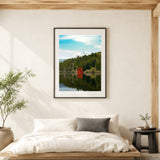 A framed art print of a Japanese landscape with a red torii gate and mount fuji reflected in a lake, displayed on a beige wall above a minimalist wooden bed in a modern, sunlit room.