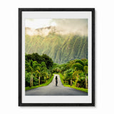 A framed art print featuring a scenic photograph of a road in Hawaii lined with palm trees and lush green mountains shrouded in mist, presented in a black frame with a white mat.
