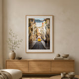 A framed art print depicting a Lisbon street scene with a yellow tram, displayed on a beige wall above a wooden console table in a styled room.