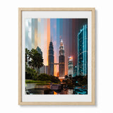 A framed art print of the Petronas Towers in Kuala Lumpur, Malaysia, featuring a colorful sunset sky with vertical gradient stripes of blue, orange, and pink. The print is housed in a light natural wood frame with a white mat, shown against a plain white background.