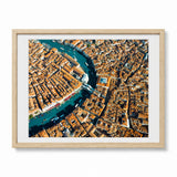 A framed aerial photograph of Venice, showcasing the Grand Canal winding through a dense city with orange-tiled rooftops and boats, presented in a light wood frame with a white mat on a white background.
