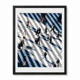 A framed art print featuring an aerial photograph of people crossing Shibuya Crossing in Japan, with a black frame and white mat on a light gray background.