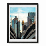 Framed art print of the Sydney skyline featuring the Sydney Tower Eye and modern skyscrapers, displayed in a black frame with a white mat.