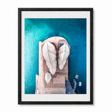 A framed aerial photograph of the Sydney Opera House, featuring the white shell-like structures over turquoise blue water, presented in a black frame with a white mat against a light gray background.