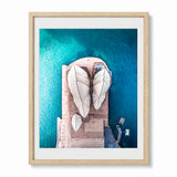 A framed aerial photograph of the Sydney Opera House surrounded by vibrant turquoise water, presented in a light natural wood frame with a white mat.