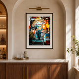 A framed vertical art print depicting a salary man walking through memory lane in Tokyo, styled on a beige wall above a wooden counter in a modern interior setting.