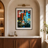 A framed vertical art print depicting a vibrant neon-lit Shinjuku scene, displayed on a beige wall in a black frame 
