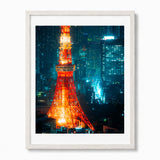 Framed wall art featuring a nighttime cityscape with the Tokyo Tower illuminated in orange-red tones against a blue-toned urban skyline, shown in a white frame on a light background.
