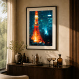 A framed vertical art print of the Tokyo Tower at night, glowing orange-red against a blue city skyline, displayed in a black frame and on a beige wall above a dark wood console table in a styled interior room.