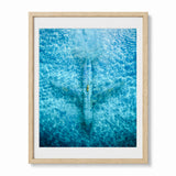 Framed wall art featuring an aerial photograph of an abandoned airplane seen from above, with rippling water patterns across the print. The artwork is presented with a white mat and a wood frame against a clean white background.